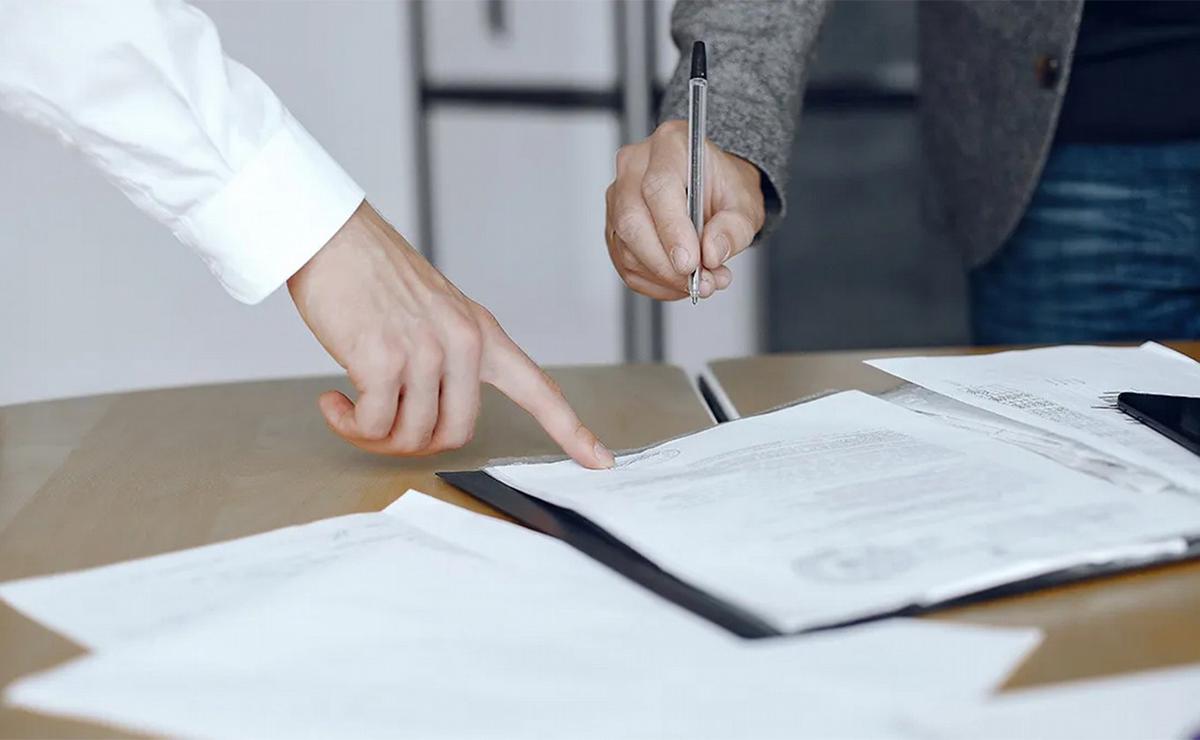 Ilustrativa.- Un hombre acerca su birome a un papel mientras otro le da indicación.